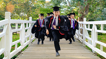 A group of grinning boys in robes run towards the camera across a white footbridge